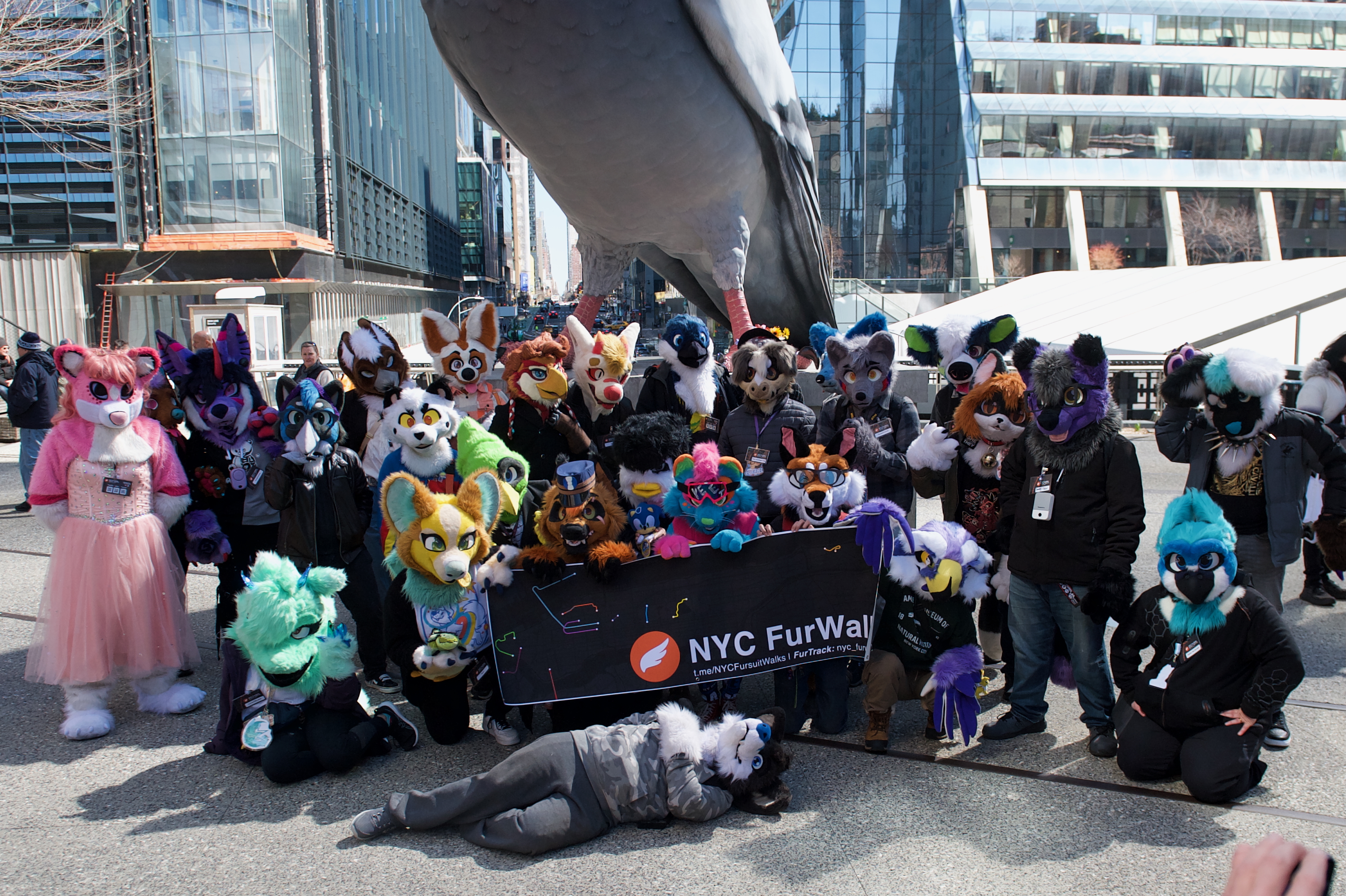 A group of over 25 fursuiters pose under a giant pigeon statue.